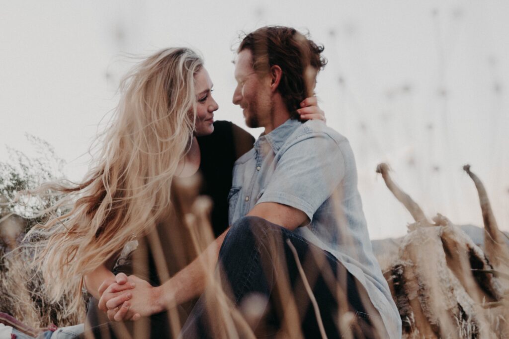 A woman and man sitting in a field looking into each others eyes.