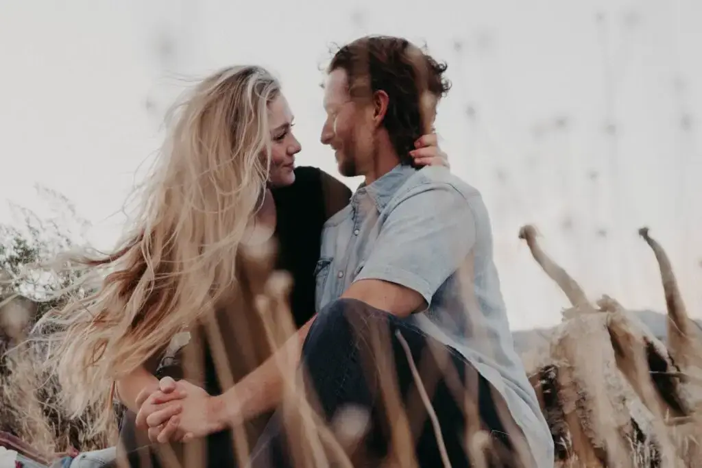 A woman and man sitting in a field looking into each others eyes.