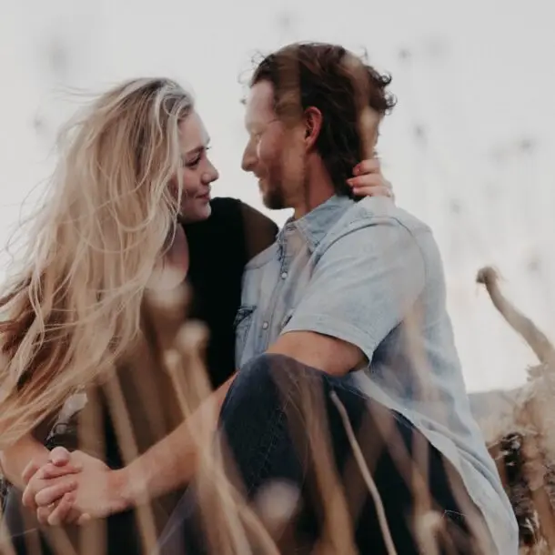 A woman and man sitting in a field looking into each others eyes.