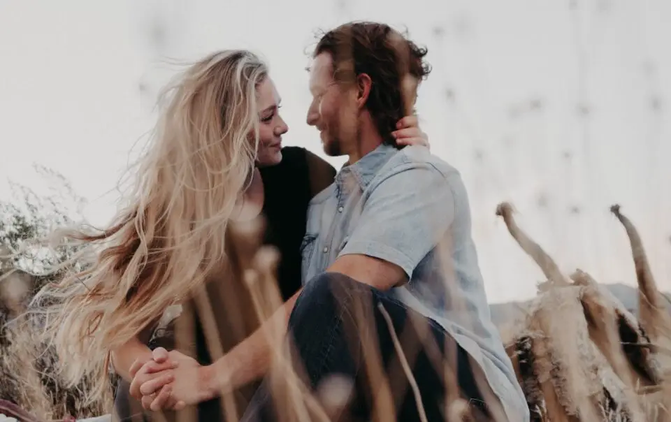 A woman and man sitting in a field looking into each others eyes.