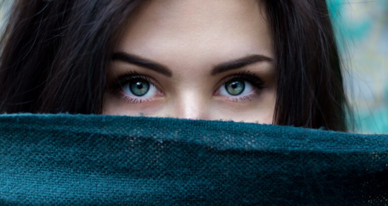 A woman looking over a blue blanket. All you can see are her green eyes.