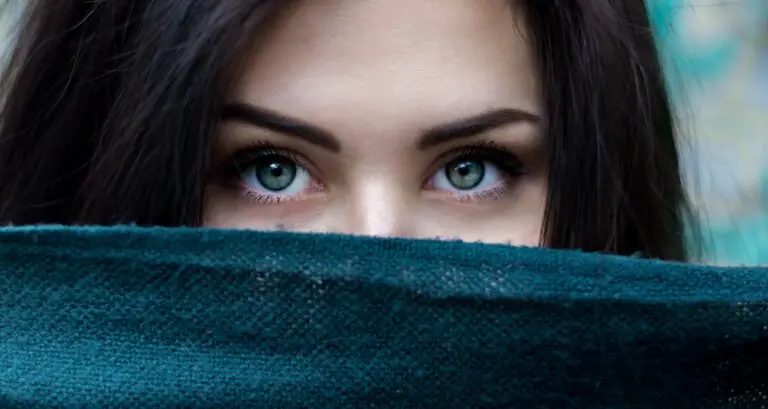 A woman looking over a blue blanket. All you can see are her green eyes.