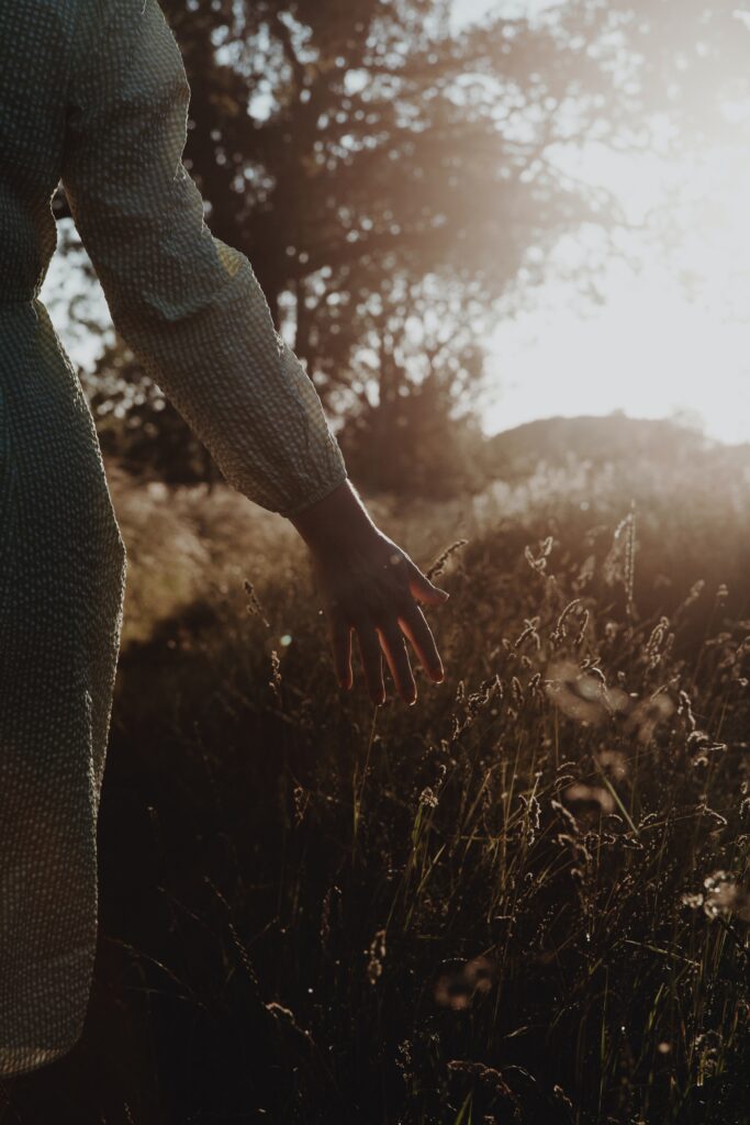 A woman with her hand against the bushes during sunset.