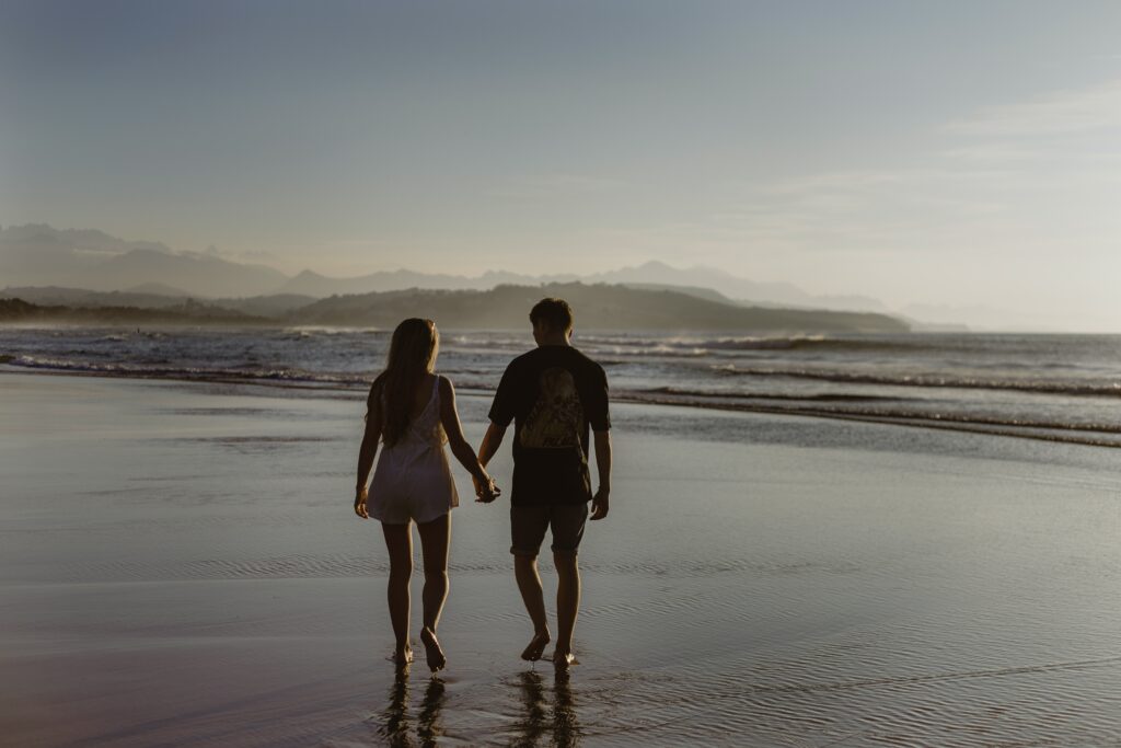A couple walking on the beach holding hands at sunset.
