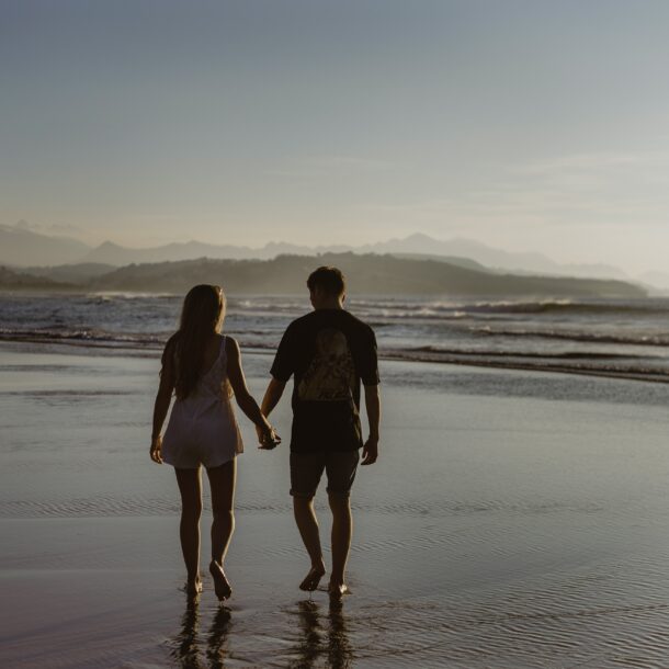 A couple walking on the beach holding hands at sunset.