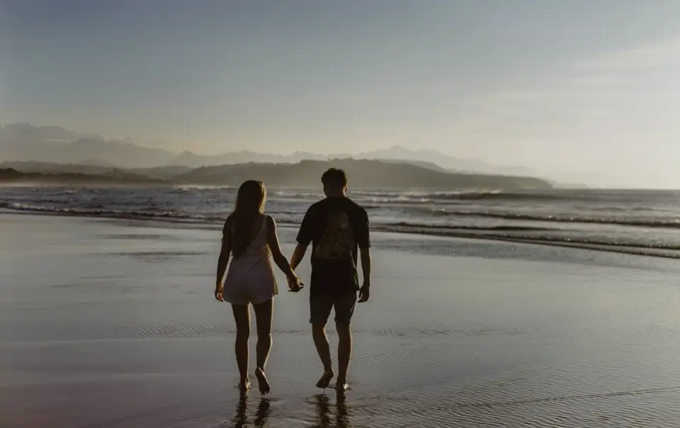 A couple walking on the beach holding hands at sunset.