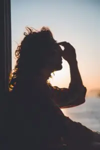 A woman's image in front of a window. She's holding the top of her nose.