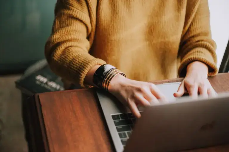 A woman in a yellow sweater typing on a computer.