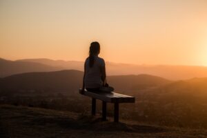A woman sitting on a bench on a mountain during sunset.