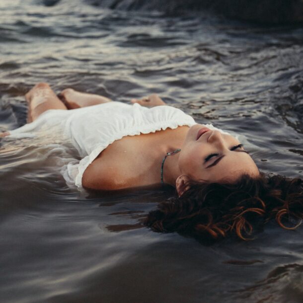 A woman in a white dress laying on top of the water.