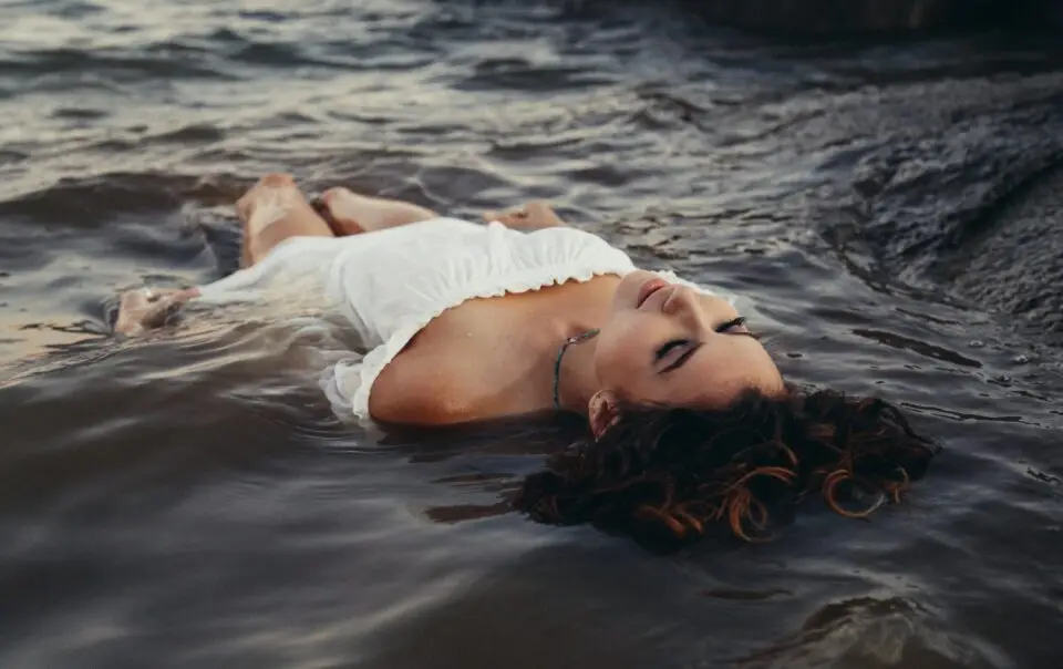 A woman in a white dress laying on top of the water.