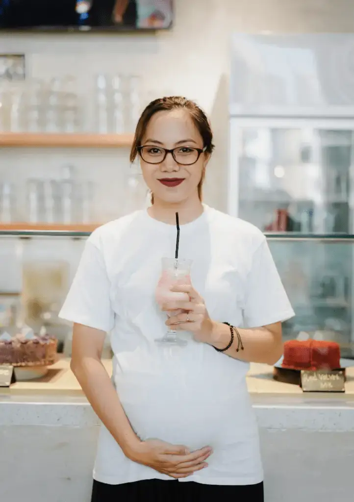 An image of a woman in a white shirt holding her pregnant stomach.